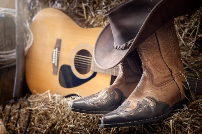 Country-Musikfestival Live-Konzert oder Rodeo mit Cowboyhut-Gitarre und Stiefel auf Scheunenhintergrund