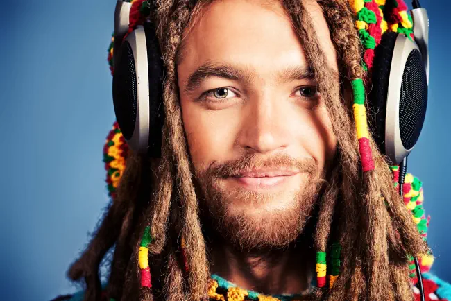 Porträt eines glücklichen rastafarischen jungen Mannes, der Musik in Kopfhörern hört.