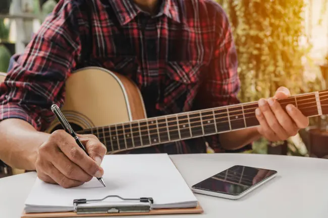 Ein Songwriter, der Stift hält, um ein Lied zu komponieren. Musiker, der akustische Gitarre spielt. Live-Musik und abstraktes musikalisches Konzept.