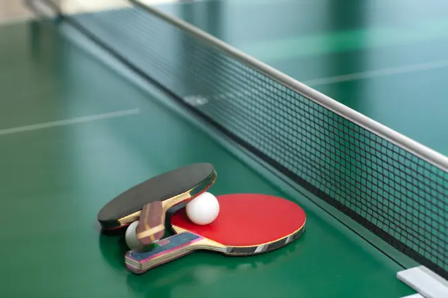 Zwei Tischtennis- oder Tischtennisschläger und Bälle auf einem grünen Tisch mit Netz