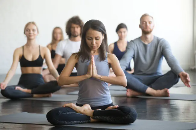 Yogalehrerin meditiert mit Schülern in einem hellen Raum.